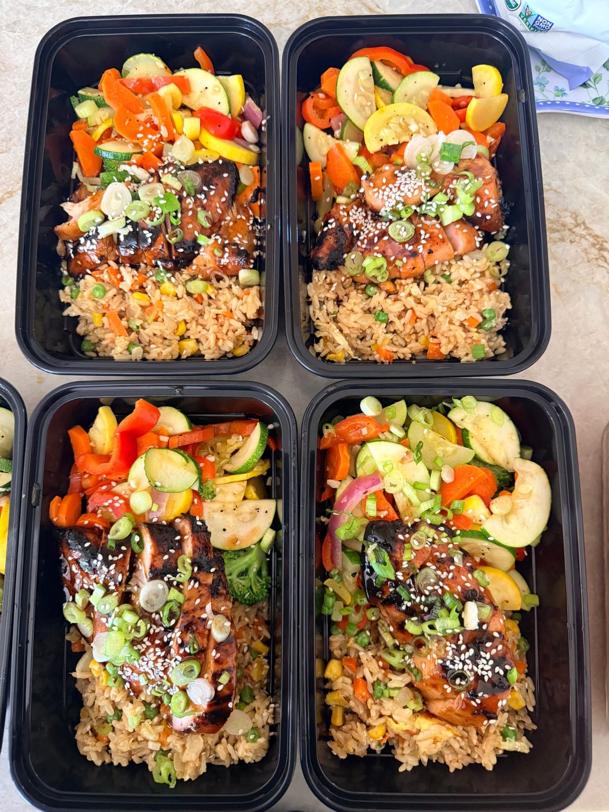 Meal prep containers of teriyaki salmon with fried rice and vegetables