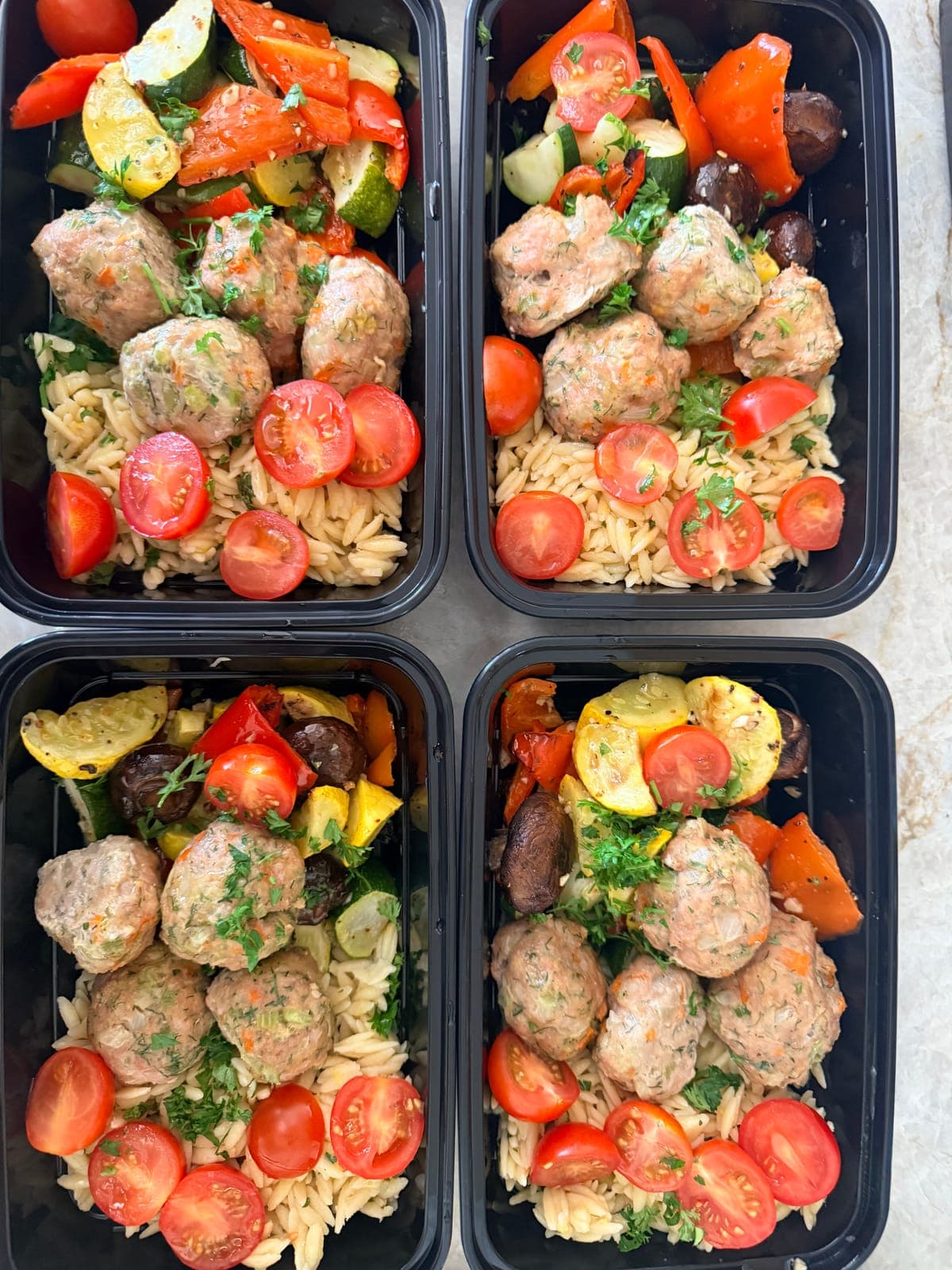 Meal prep containers of turkey meatballs with orzo, tomatoes and roasted vegetables